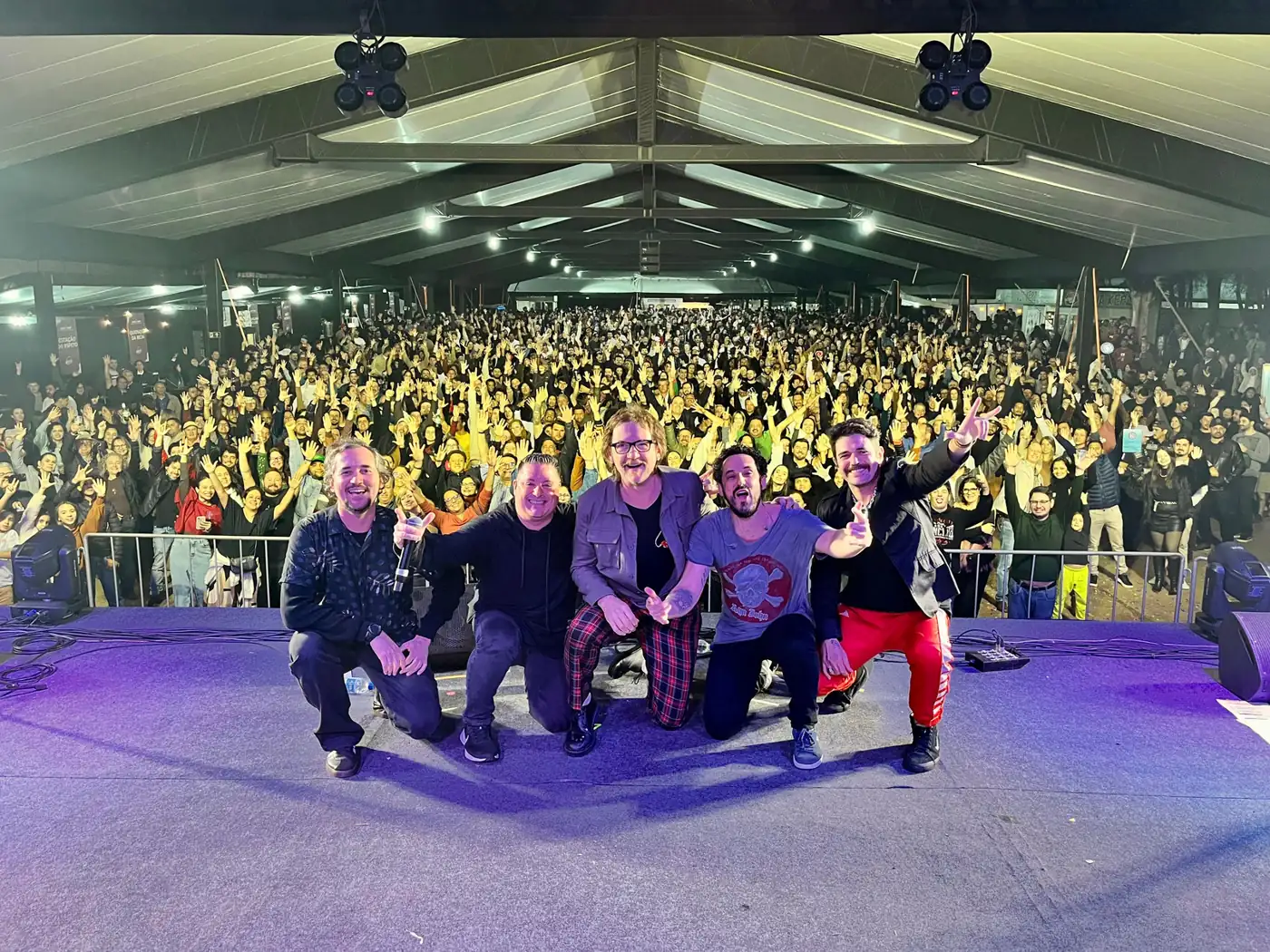 Músicos do projeto Amigos do Rock no palco, com o público lotando o espaço