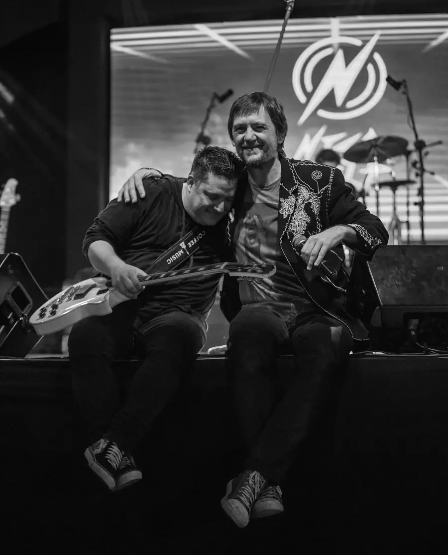 Tiago Adorno abraçado a outro músico no palco, em preto e branco